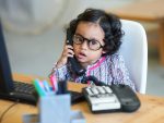 little girl sitting in front of a computer while talking on the phone