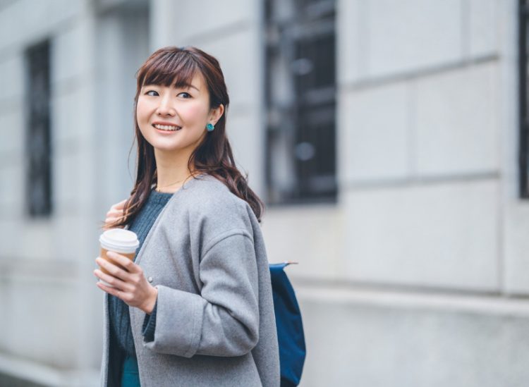 A businesswoman is walking in the street while holding a coffee cup.
