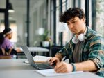 Young student taking notes while e-learning on laptop