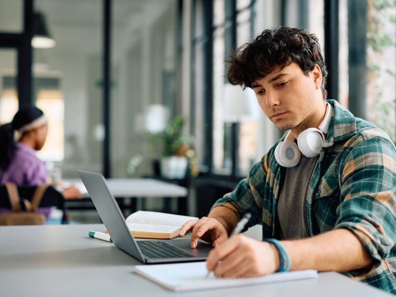 Young student taking notes while e-learning on laptop