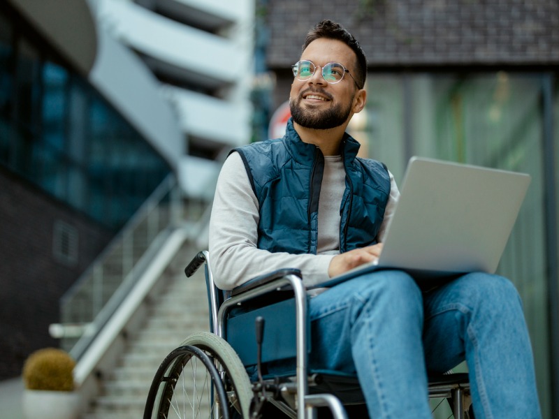 Man in wheelchair working on a laptop outside