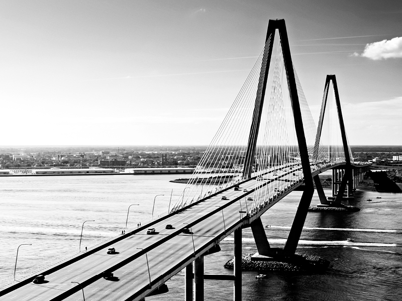 Black and white photo, large bridge with cars on it, over water.